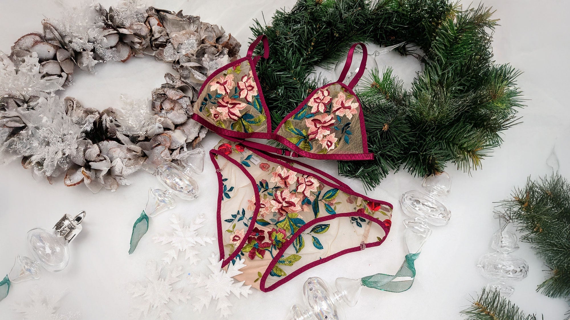 Embroidered luxury lingerie set in red and pink flowers, laid flat on a table with 2 christmas wreaths and glass ornaments