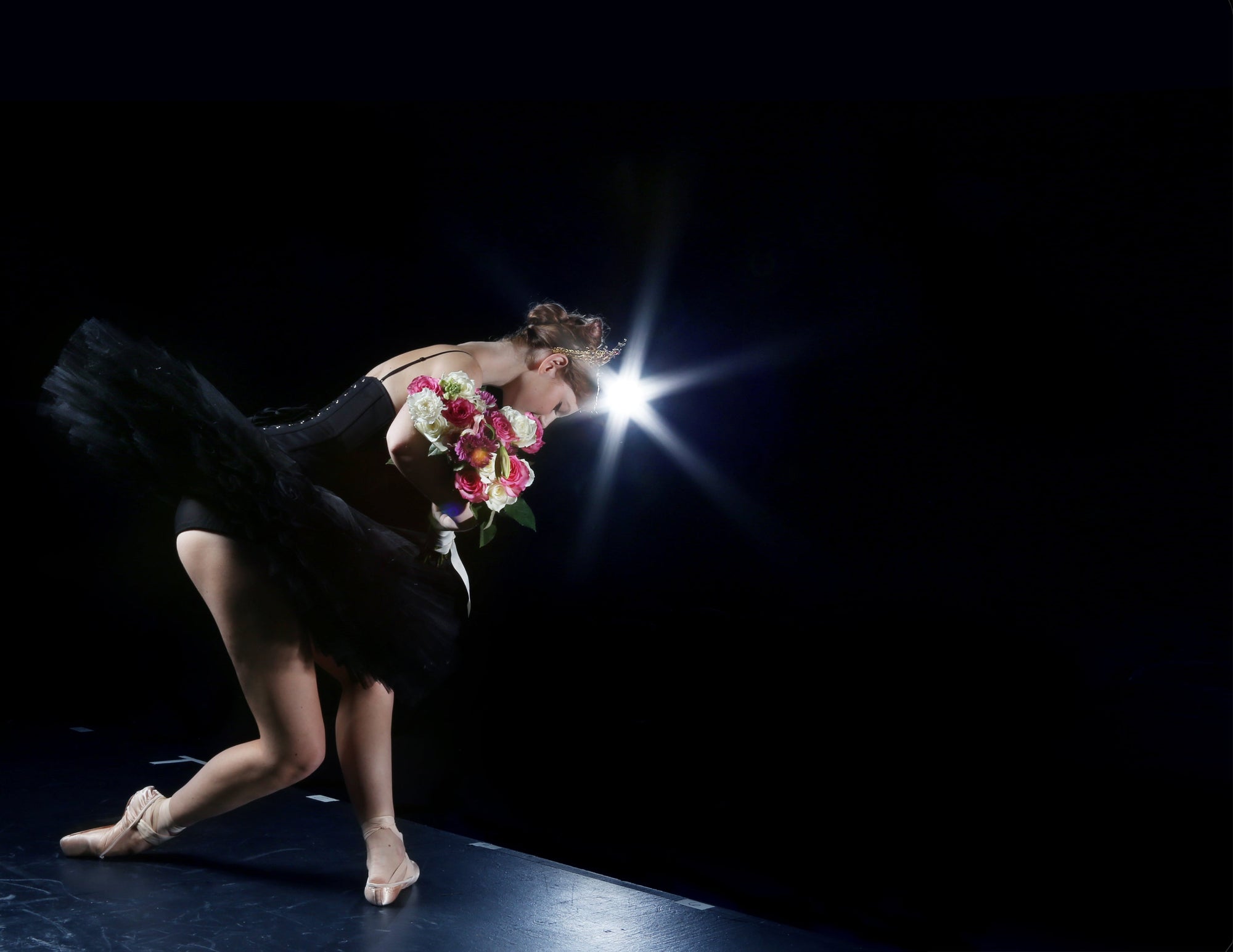 Ballet dancer in a black tutu and corset, with floral bouquet taking her final bow after the performance