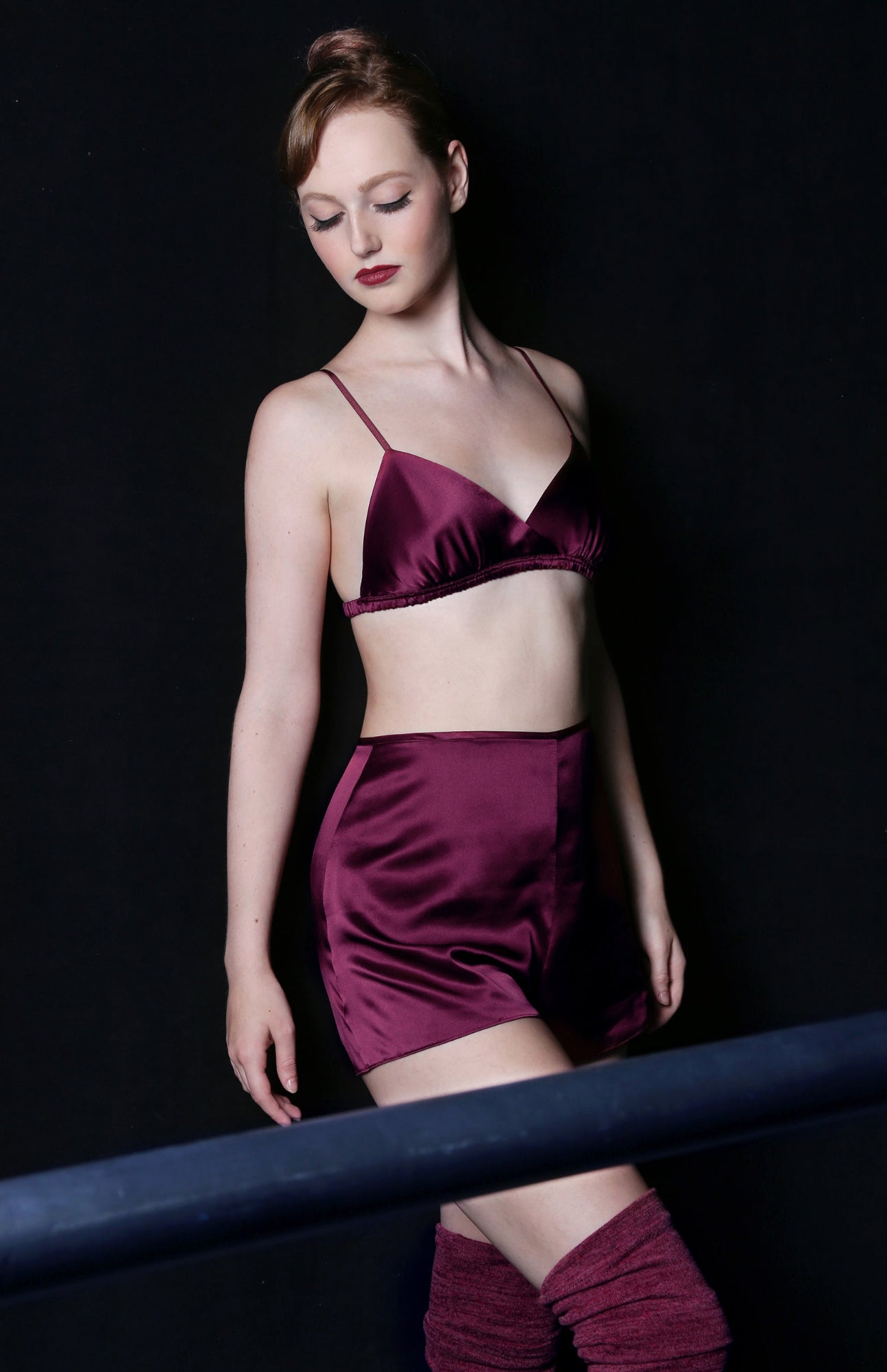 Ballerina at the barre, wearing a maroon silk bralette, tap pants, and leg warmers