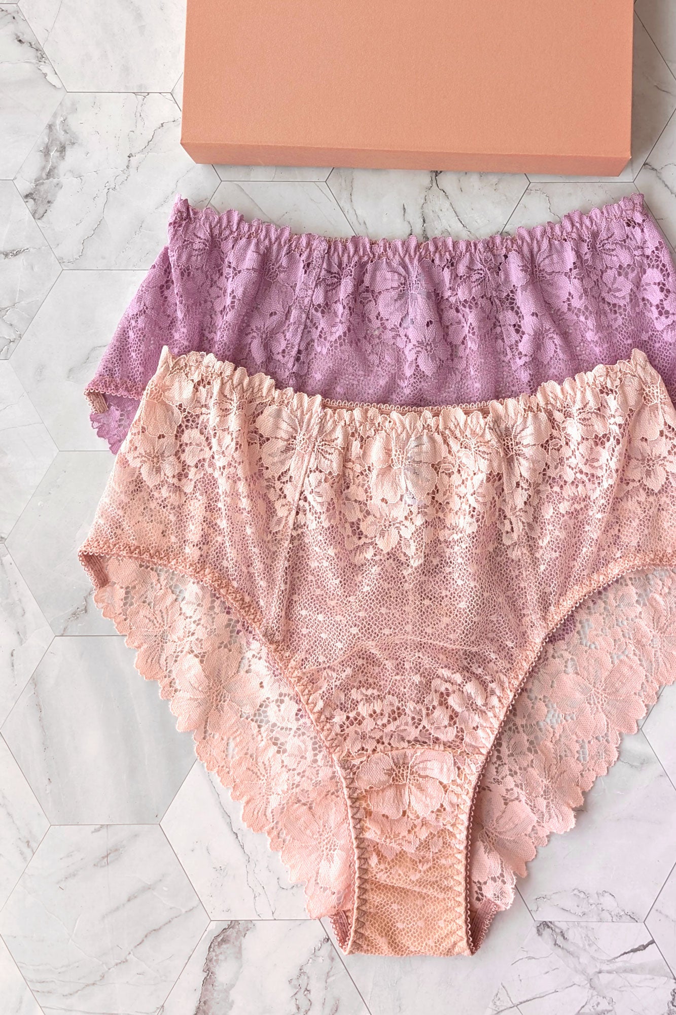 Two pairs of designer lace underwear, one pink and one purple, with modern hi-waist cuts and soft scalloped edges