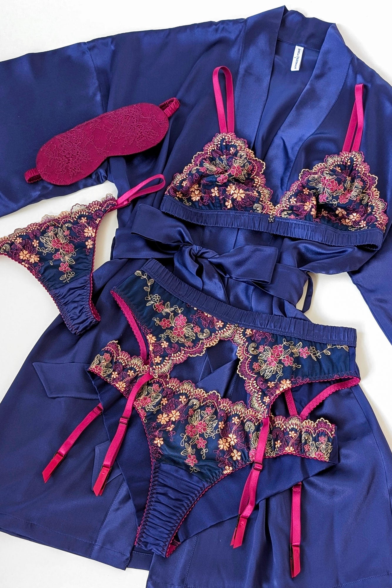 Flat lay of a luxury blue silk robe with a floral lingerie set and pink lace sleep mask