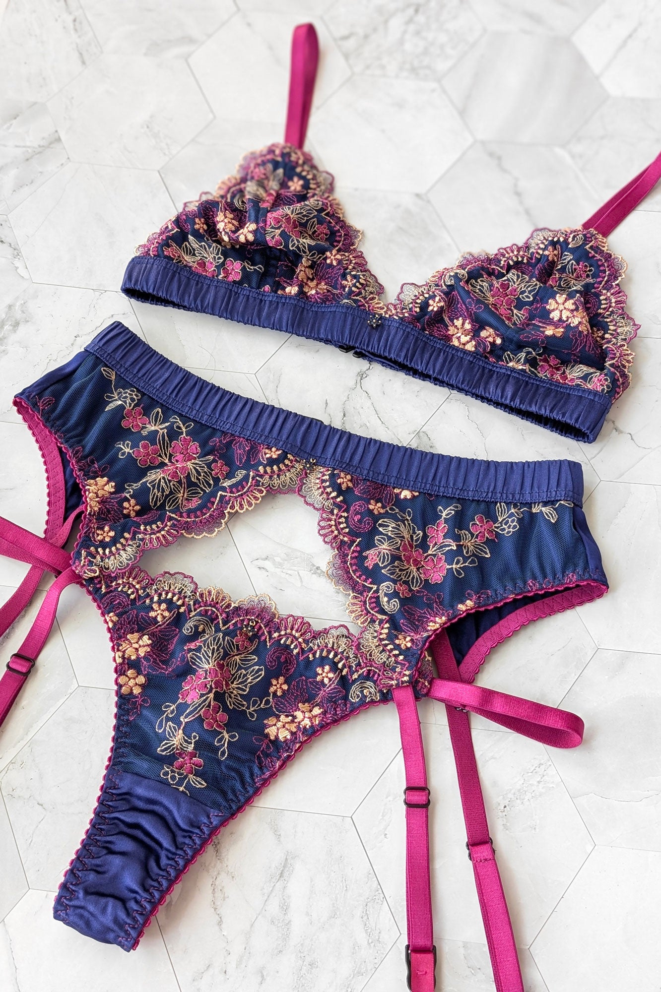 Embroidered lingerie set with pink straps and pink and navy floral stitching on a white marble background