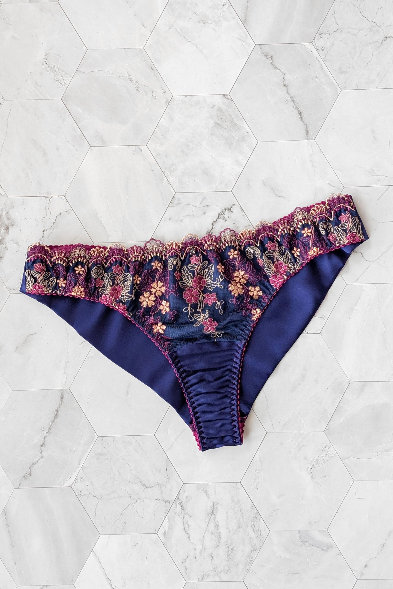 Navy blue underwear with floral scalloped lace trim and silk linings on a white marble background