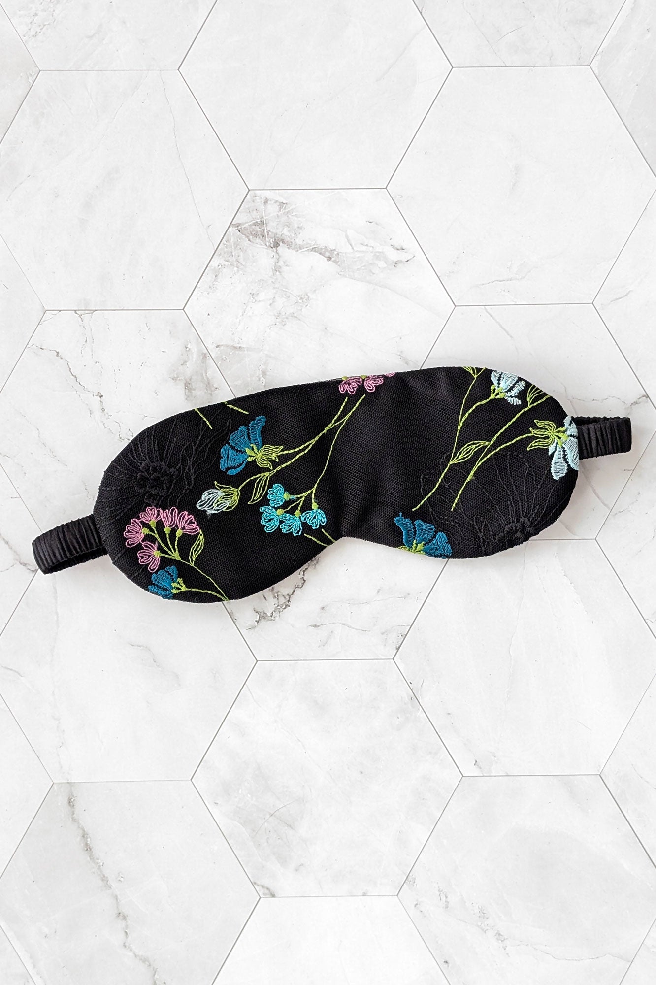 Black sleep mask with floral embroidery on a white marble surface