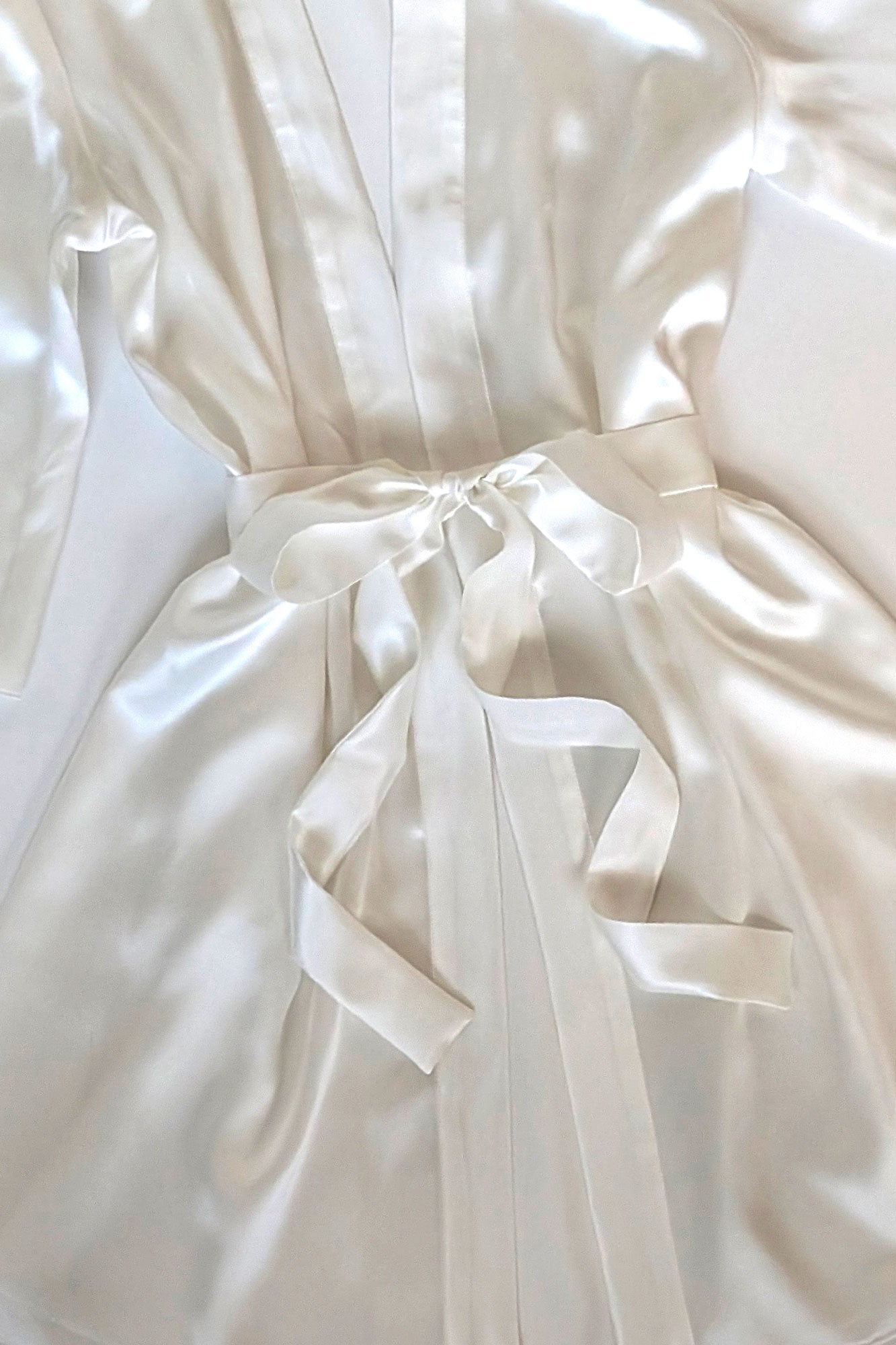 Close up of a white satin wedding robe with a ribbon belt tied into a bow