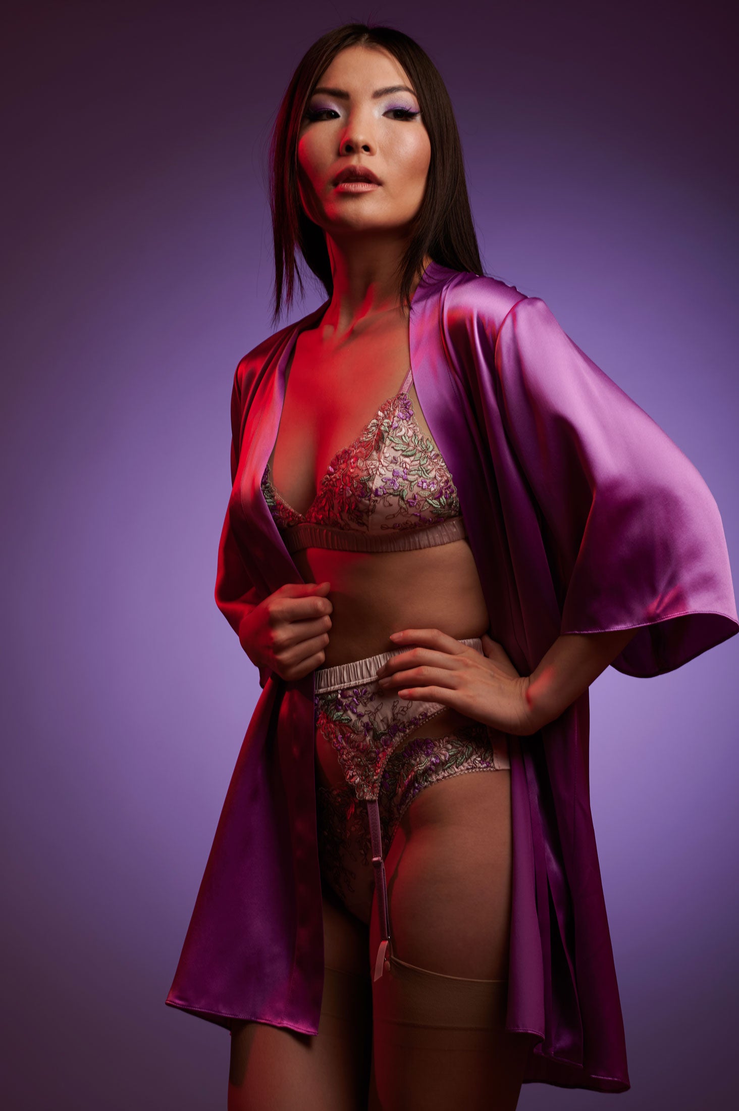 Woman wearing a purple silk robe over a 3 piece luxury lingerie set, against a purple background
