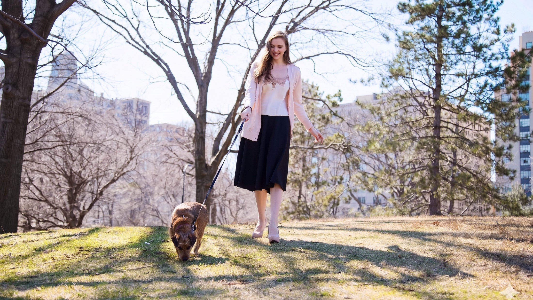Woman in a pink silk camisole and cardigan walking a dog in central park