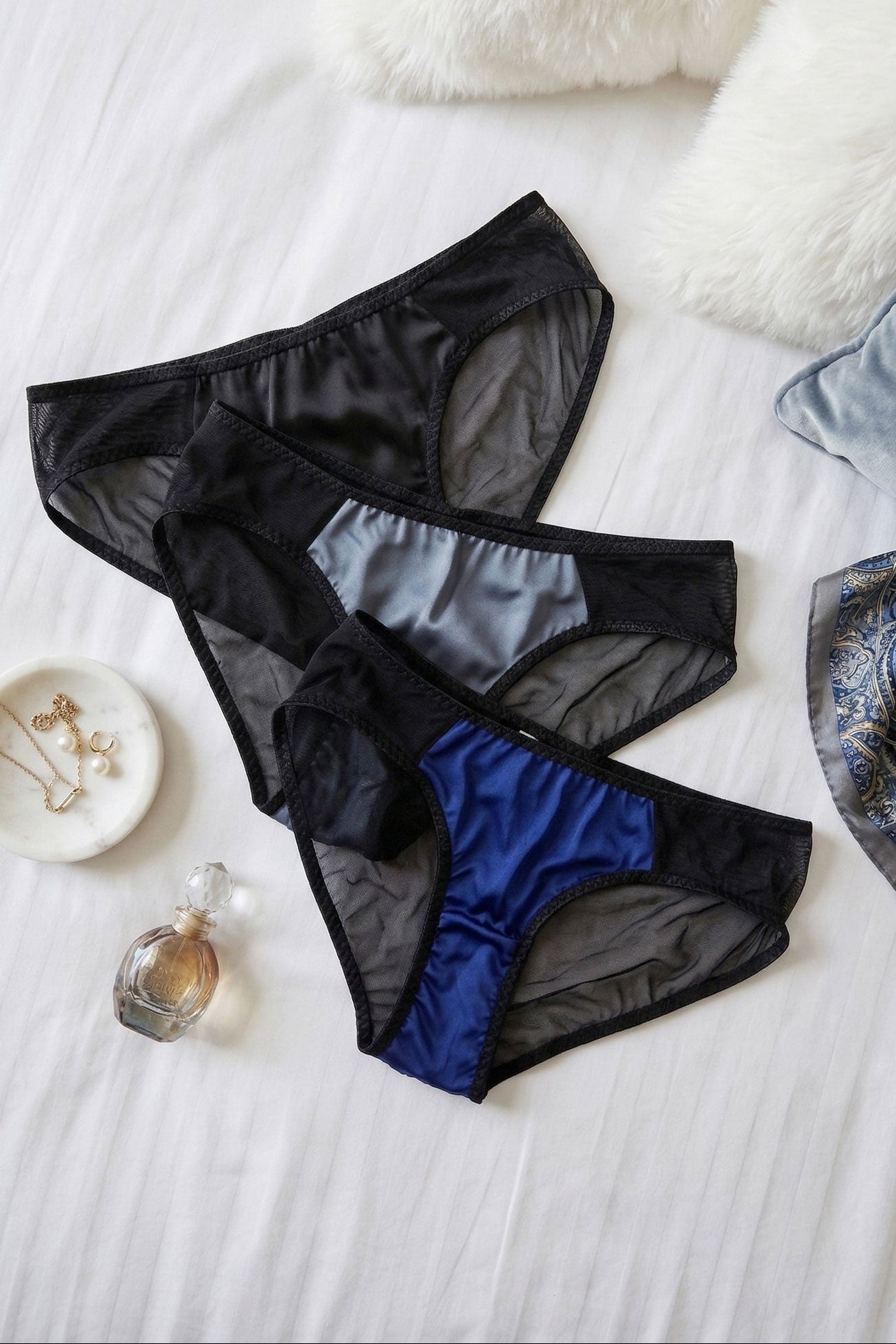 Black and blue sheer mesh underwear on a bed with gold jewellery and a perfume bottle