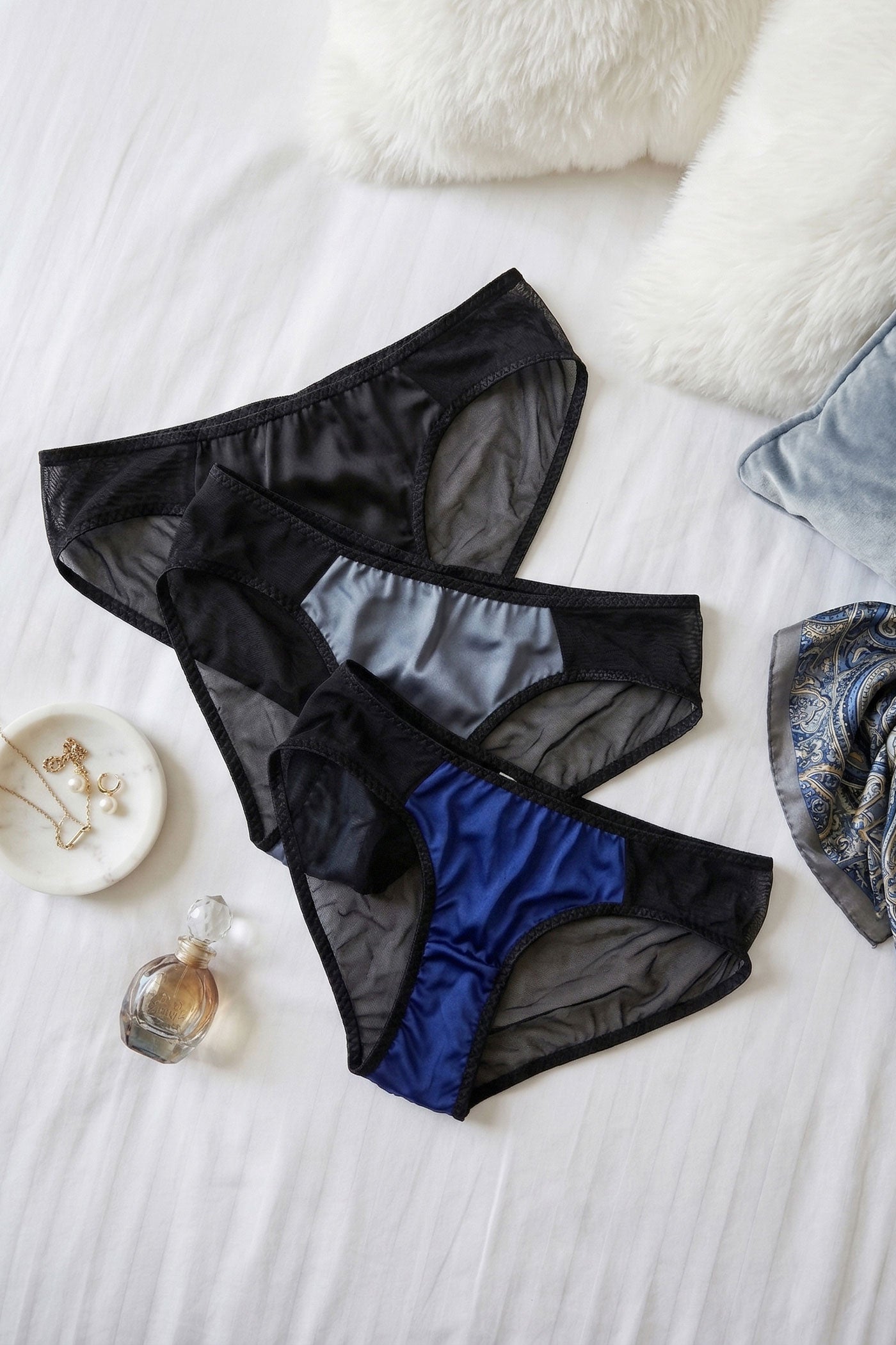 Black and blue sheer mesh underwear on a bed with gold jewellery and a perfume bottle