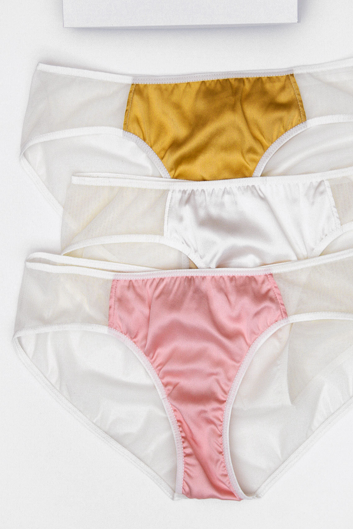 Three pairs of silk underwear in white, gold, and pink with ivory mesh backs