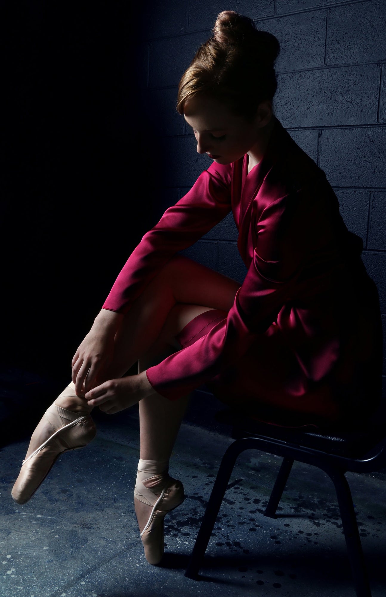 Ballerina in a red silk robe sitting on a chair, tying her pointe shoes