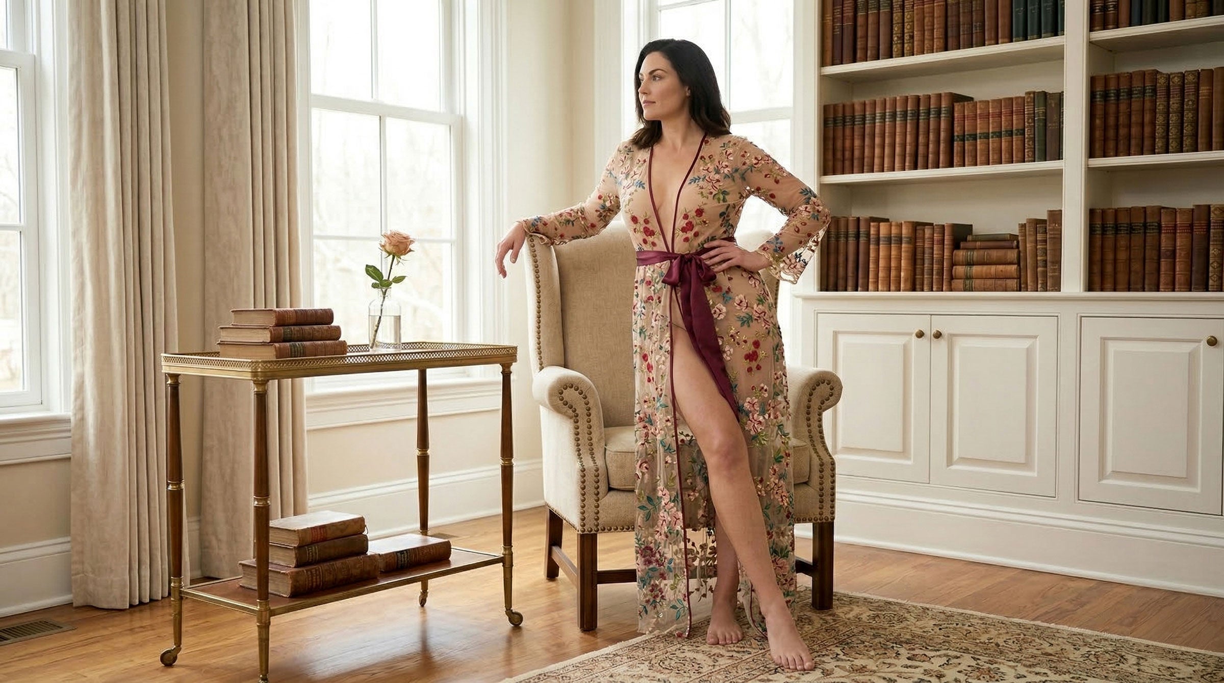 Woman in a floral dress standing in a room with a large antique bookcase and upholstered armchair