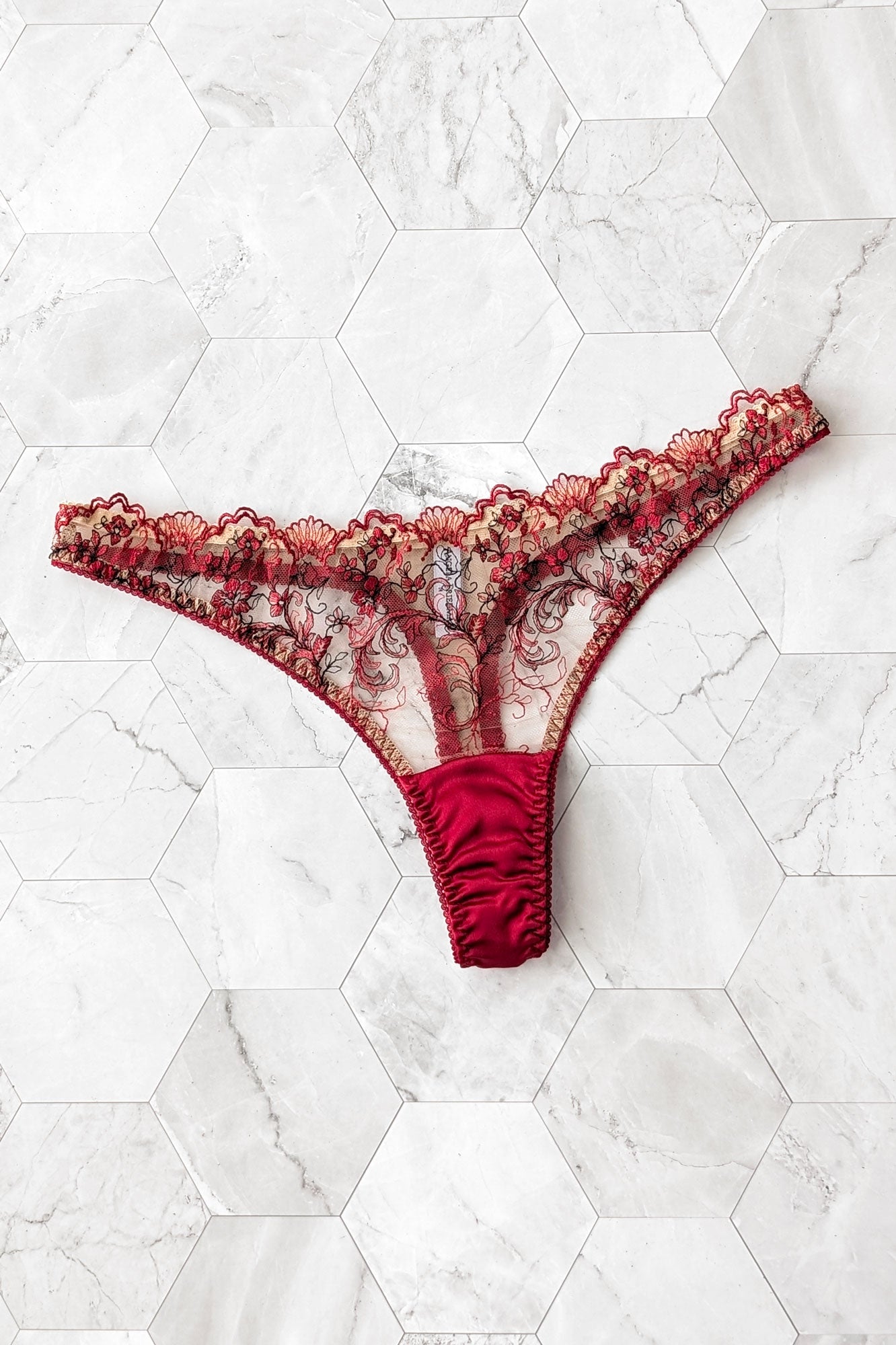 Red lace thong with a silk gusset on a white marble background