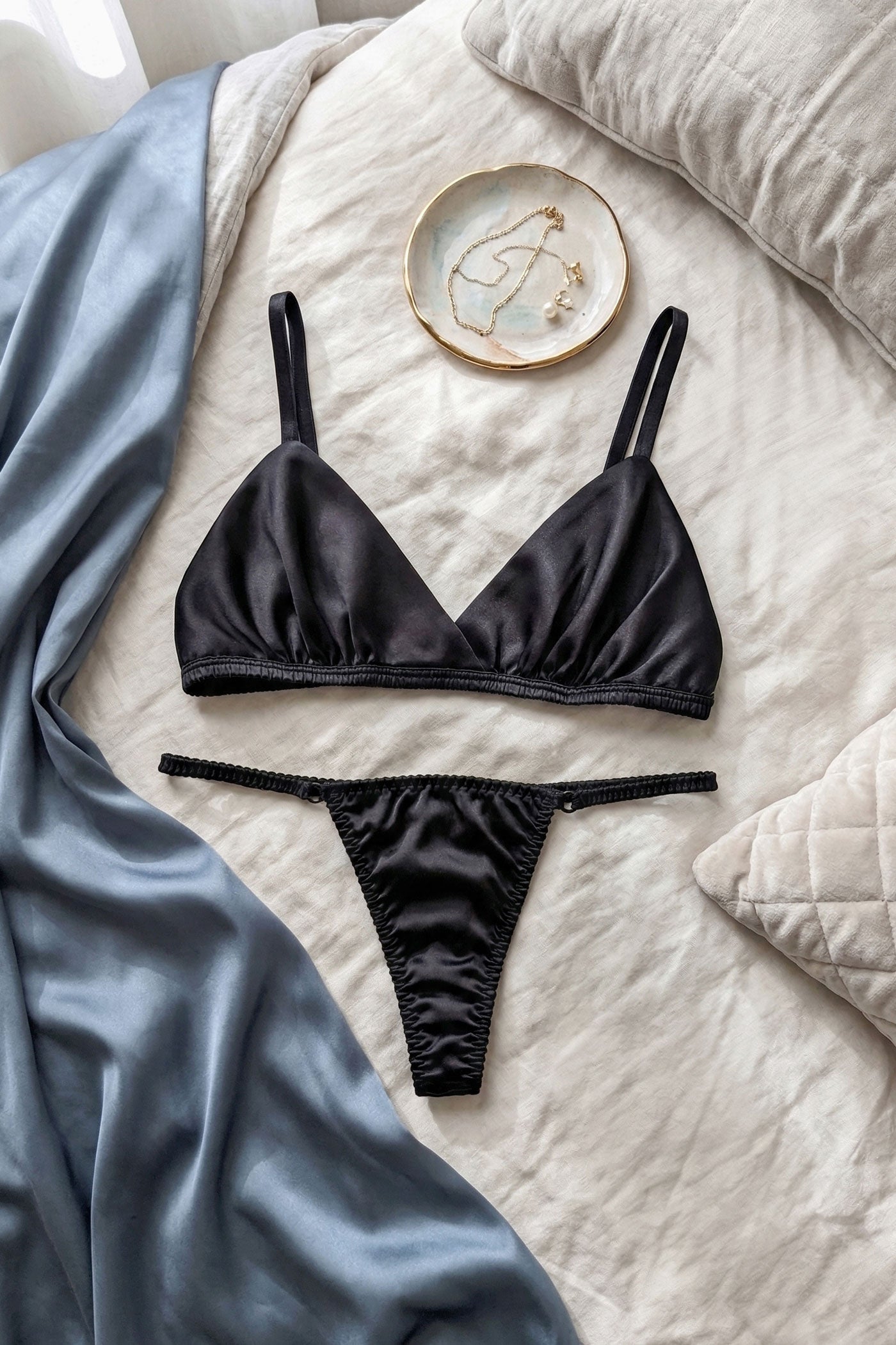 Flatlay of black silk satin bralets and silk thongs by luxury lingerie designer Angela Friedman