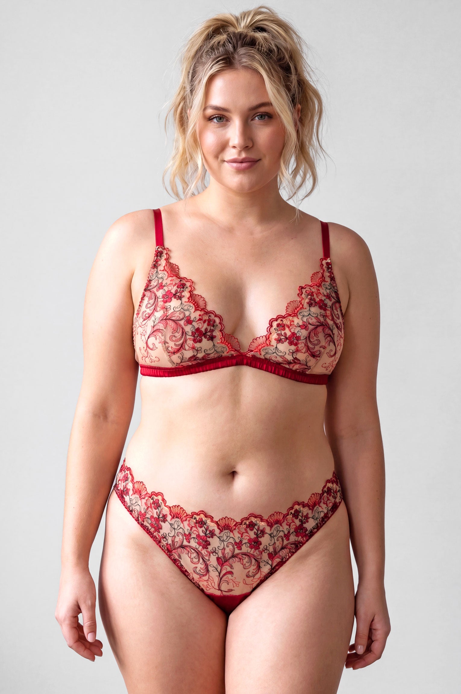 Plus sized model wearing a red sheer lace lingerie set with wireless bralet and high leg panties