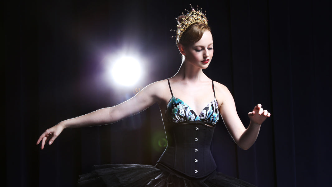 Ballerina in a gold tiara, wearing a black corset and silk floral bralette and tutu skirt