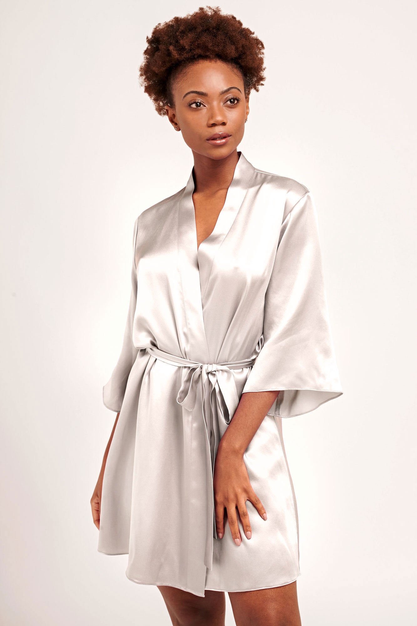 A bride wearing an off-white, silk satin robe with a tied sash belt and bow