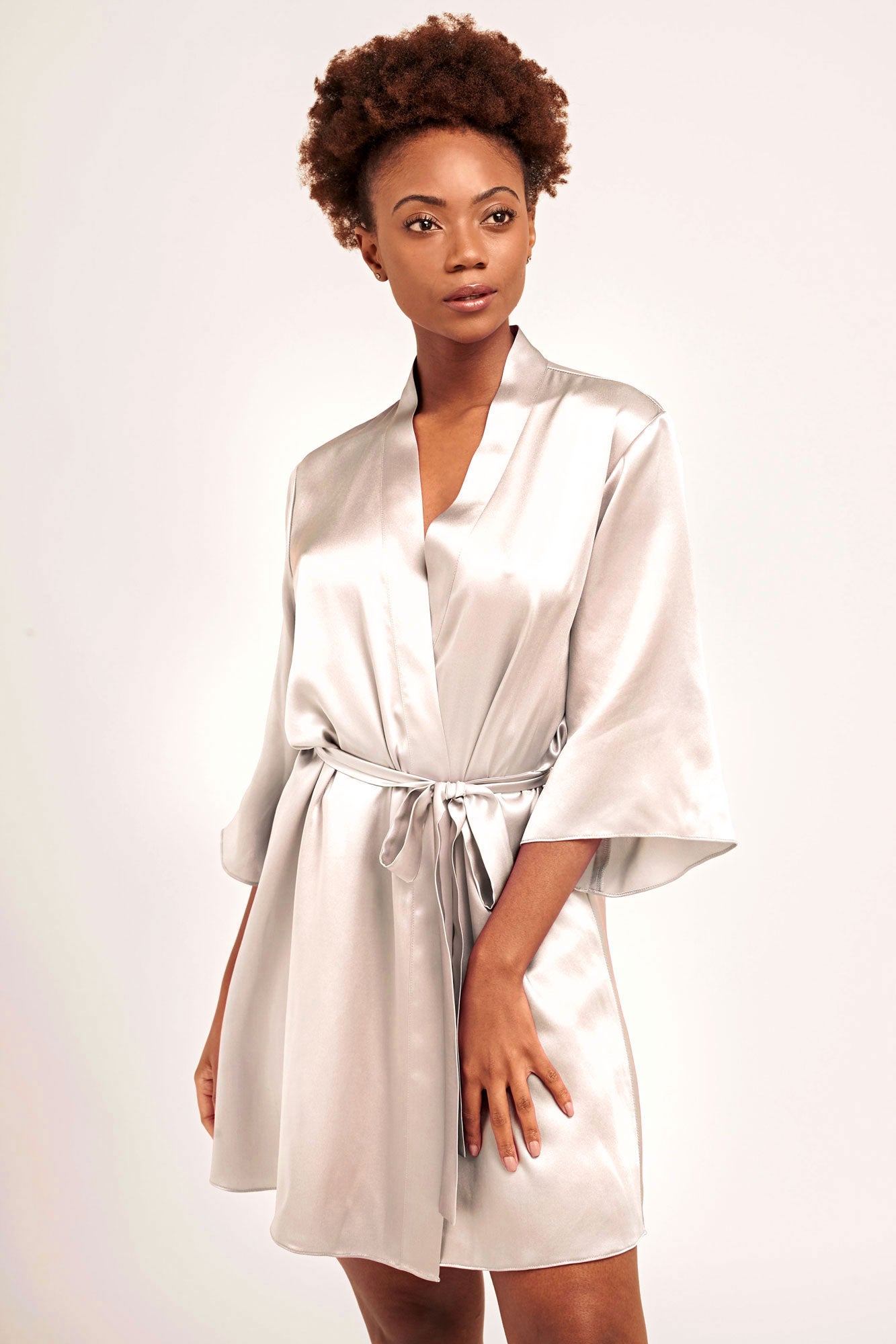 A bride wearing an off-white, silk satin robe with a tied sash belt and bow