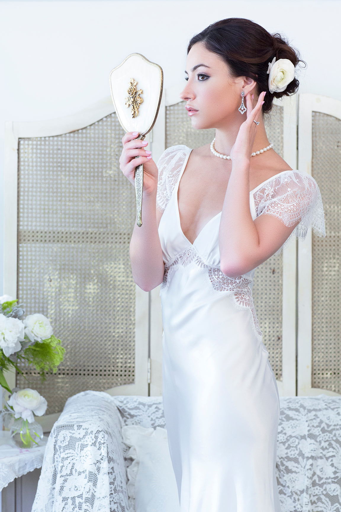 Bride getting ready for her wedding day in a white silk bias-cut gown with lace insets and a string of pearls